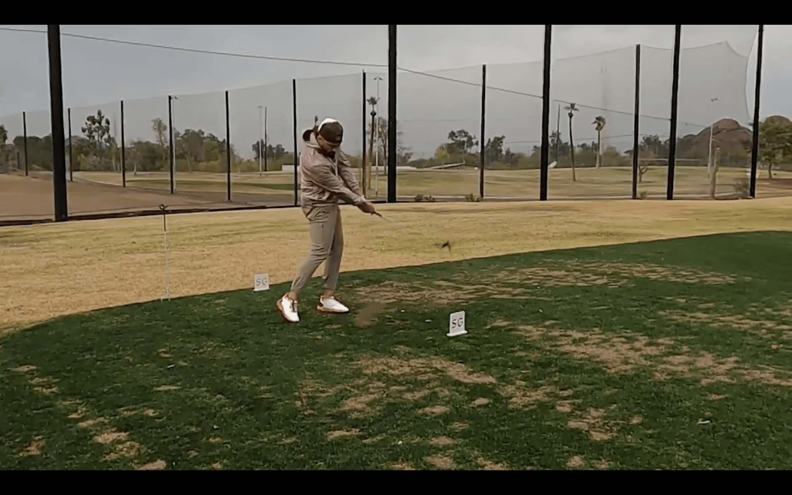 Golfer swinging club on driving range.