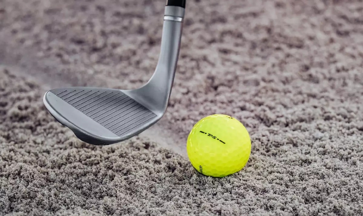 Golf club and ball on sandy surface