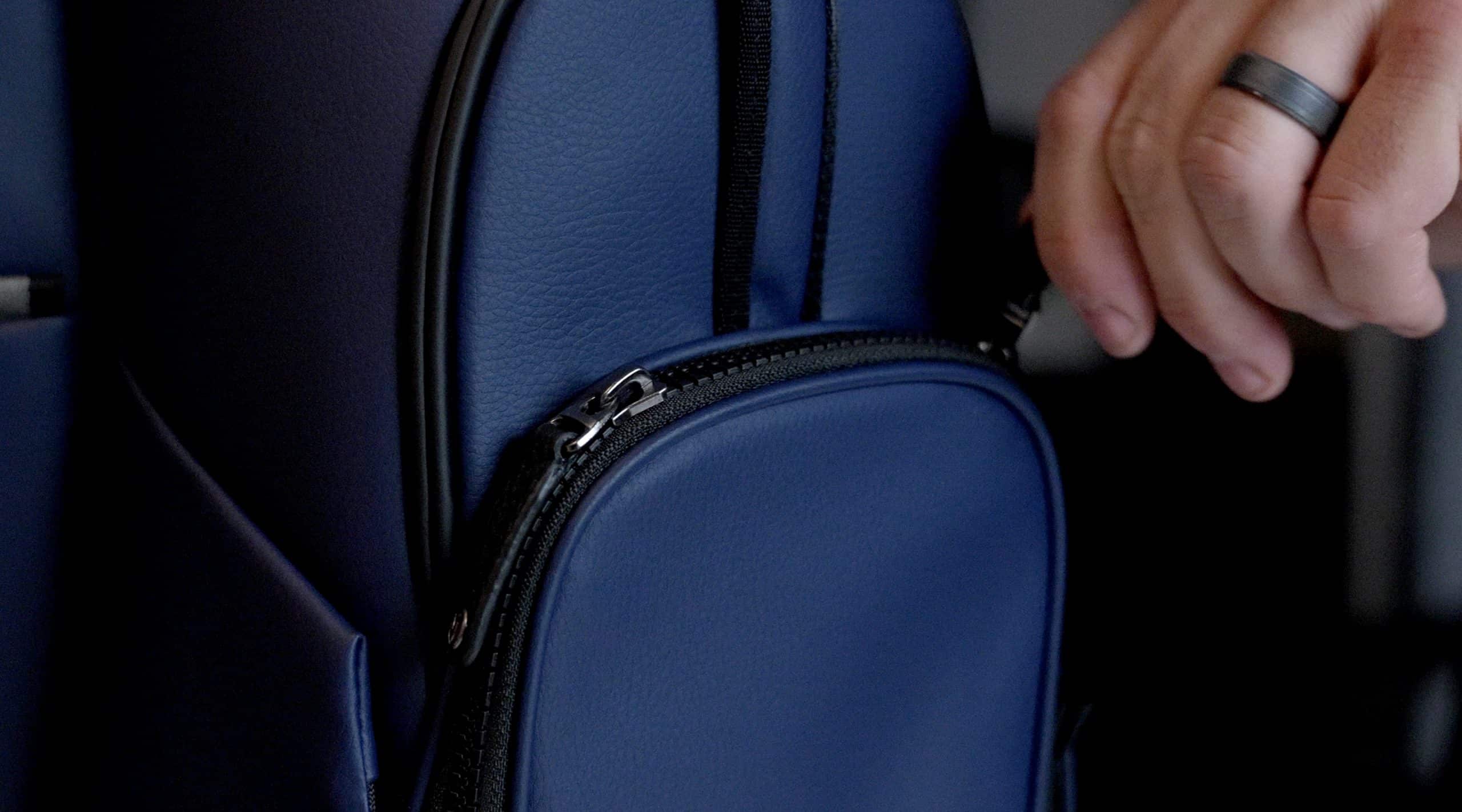 Hand unzipping blue leather backpack pocket