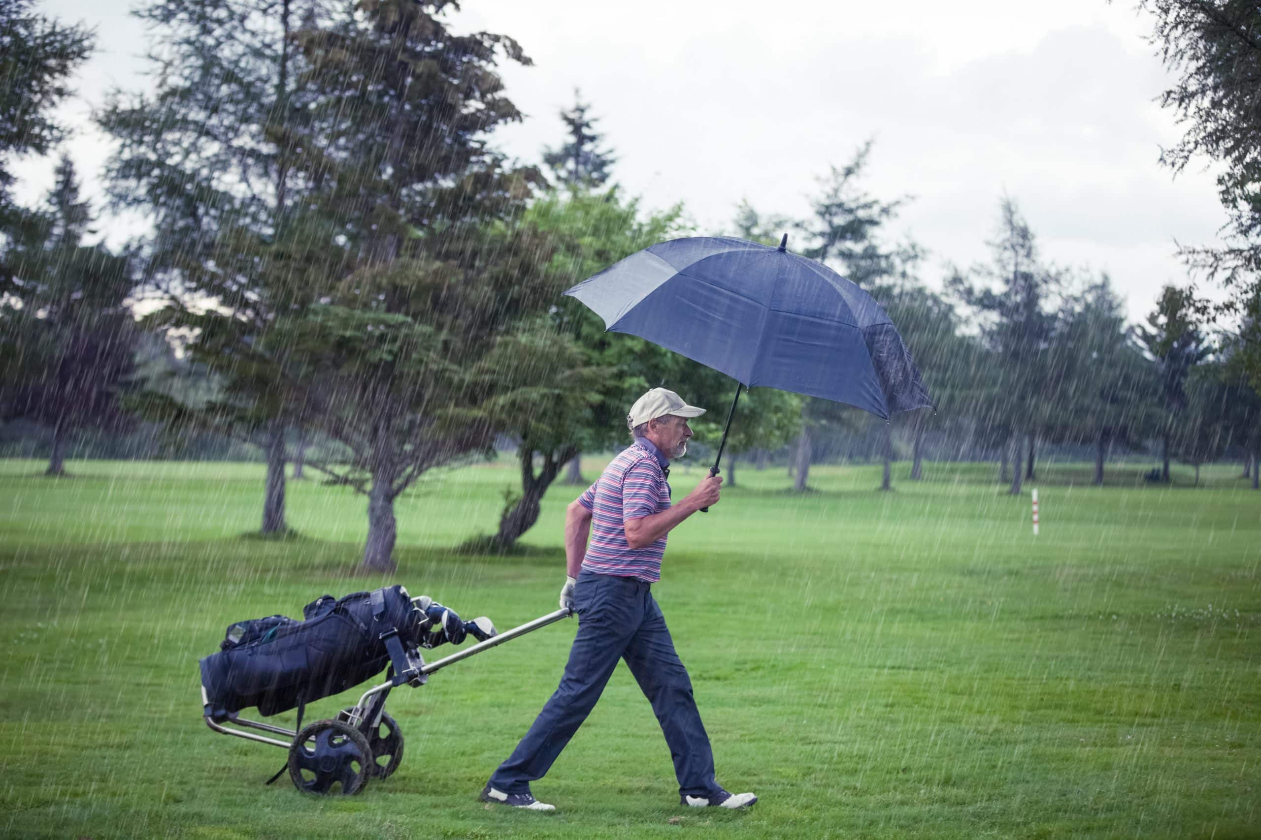 Golfer walking in rain holding umbrella