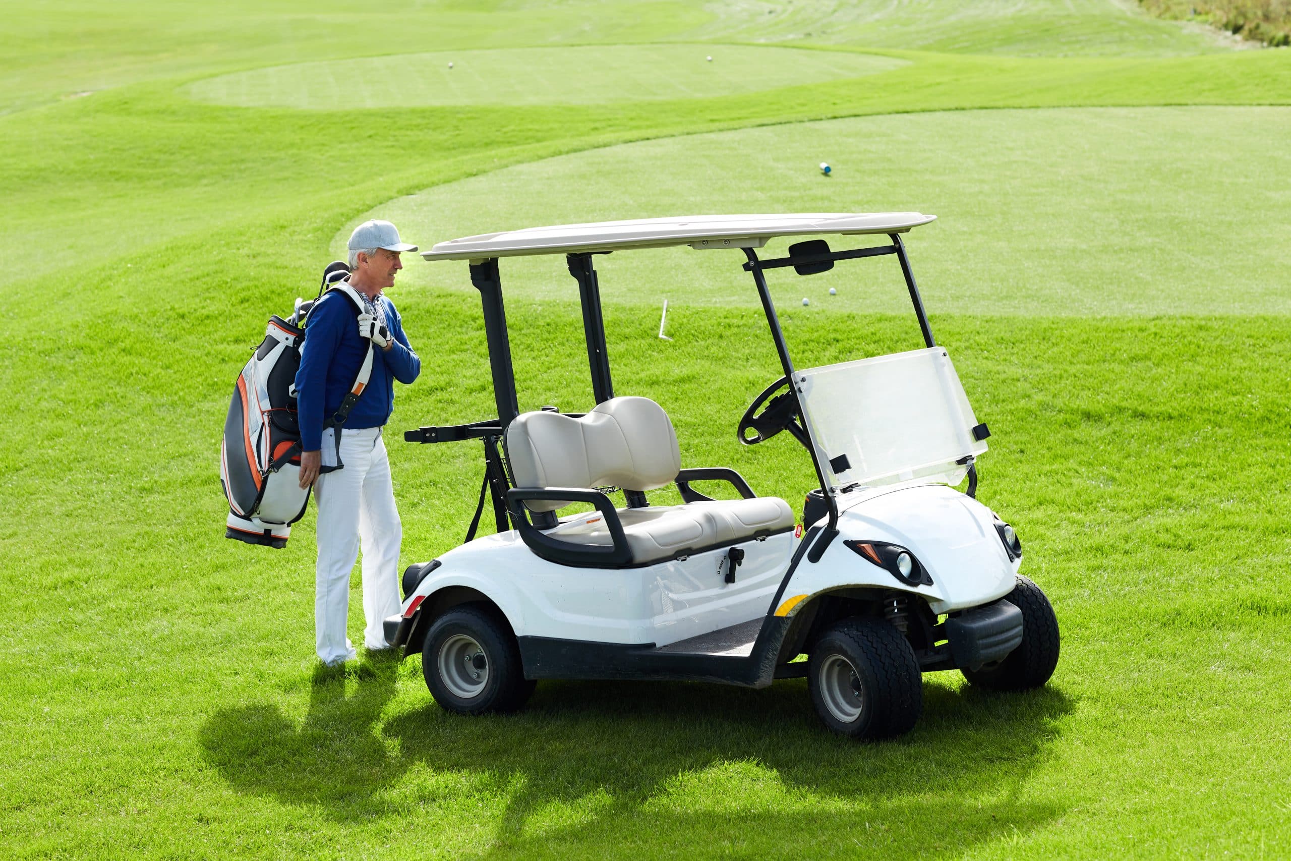 Golfer standing beside golf cart on course