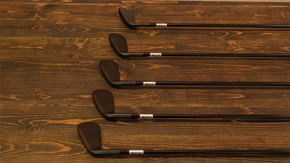 Five black golf clubs on wooden surface