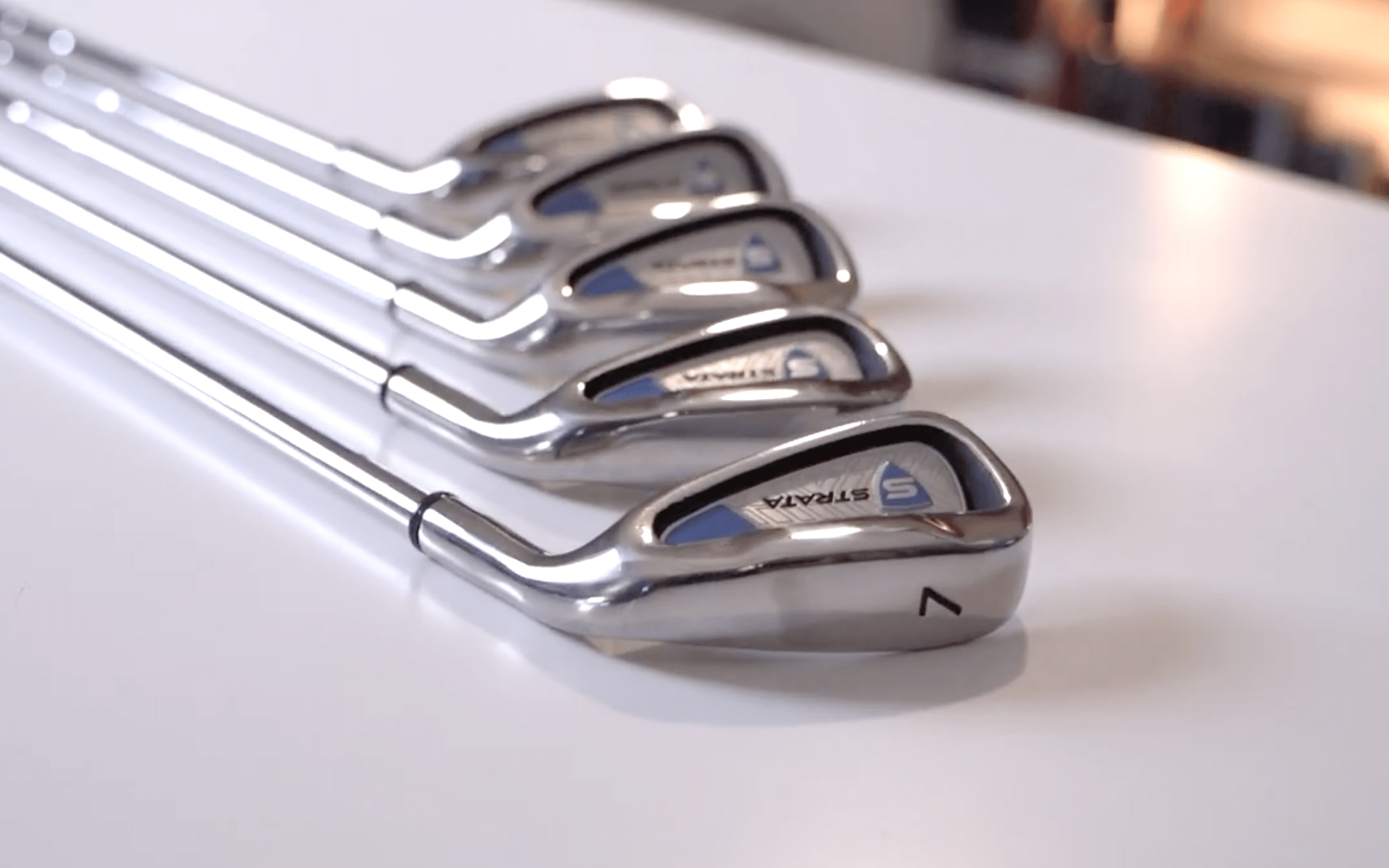 Set of silver golf irons on white surface