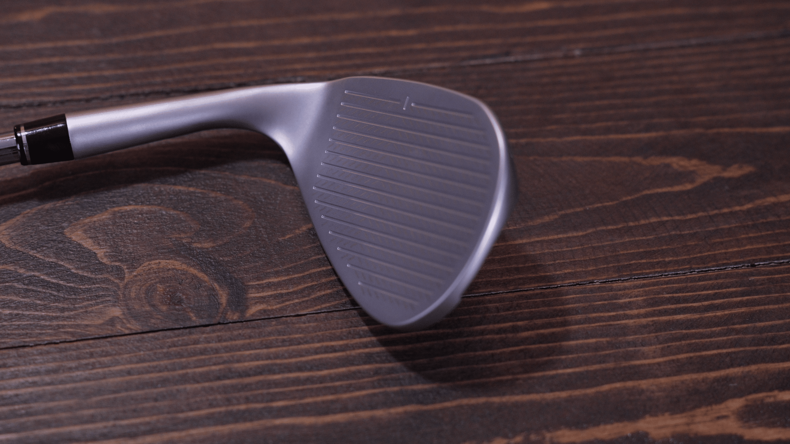 Close-up of golf wedge clubface on wood surface