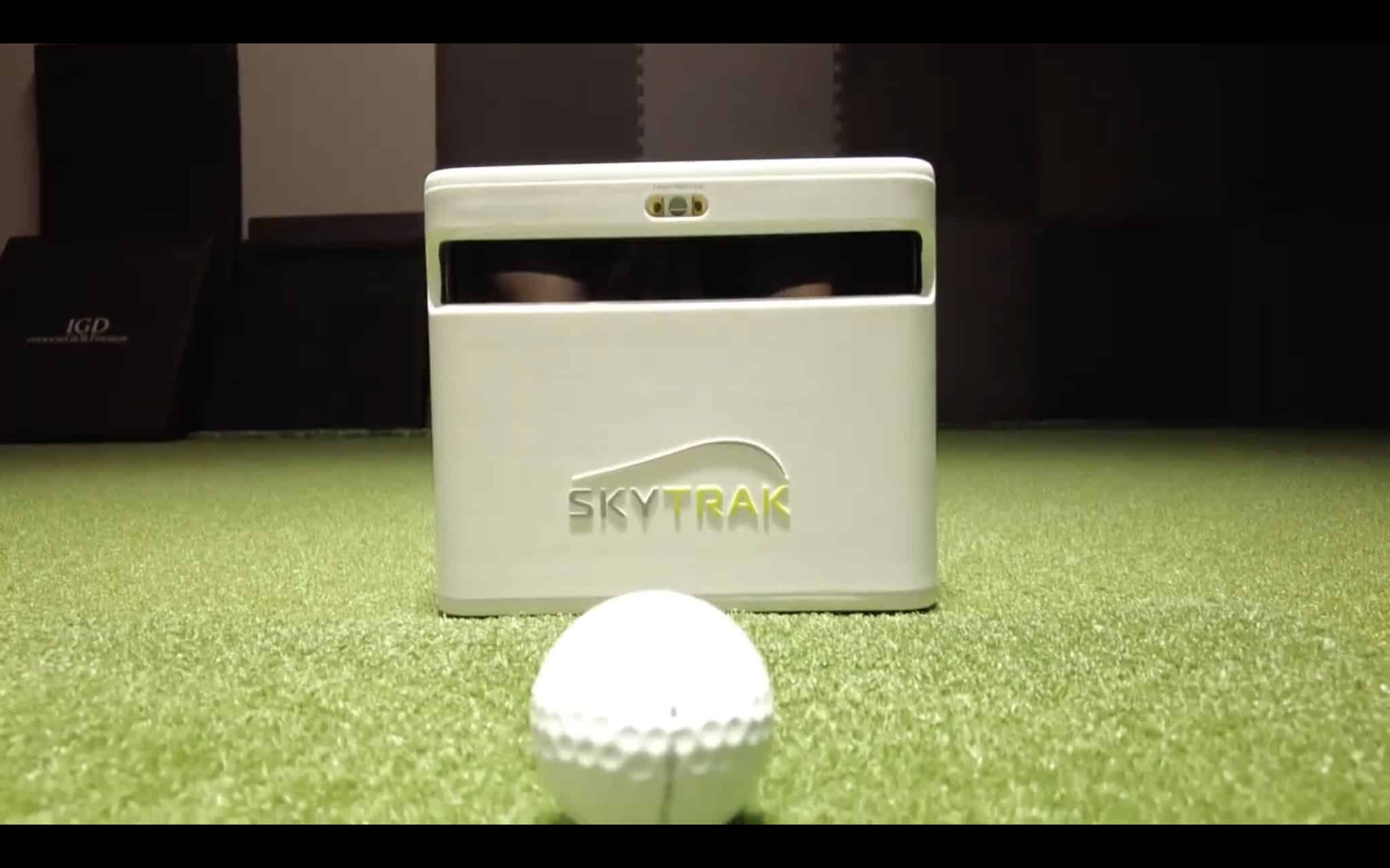 SkyTrak+ launch monitor sitting on turf next to a golf ball